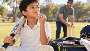 Boy in cricket whites applying a Dirty Good Berry Blast chapstick from the Zest & Zing Duo at the park