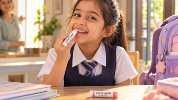 Girl in school uniform applying Dirty Good Strawberry Kids Chapstick, with Watermelon Kids Chapstick from the Fruit Pop Pair on the table